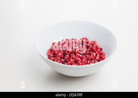 Superfood pomegranate seeds in a white bowl on a plain white surface and background. Stock Photo