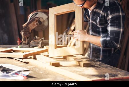 Carpenter working on woodworking machines in carpentry shop. A man works in a carpentry shop. Stock Photo