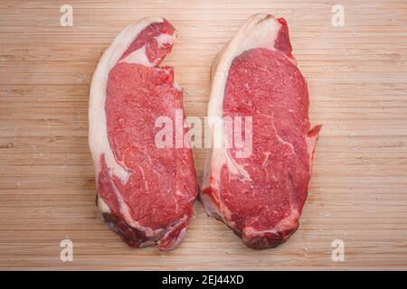 Two raw dry aged marbled sirloin steaks seasoned with salt on a wooden chopping board. Stock Photo