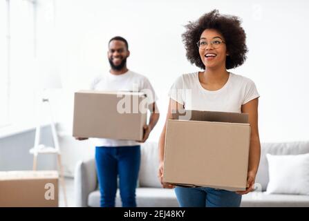 Joyful Black Spouses Carrying Moving Boxes Entering New Home Together Stock Photo