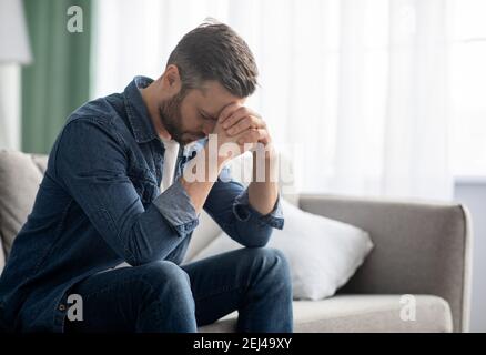 Depressed man sitting on couch in living room Stock Photo