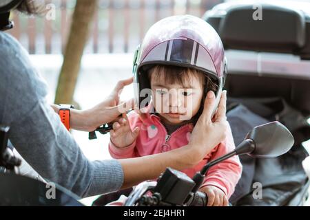 little baby wears a motorcycle helmet when fastened by its mother on the motorbike Stock Photo Alamy