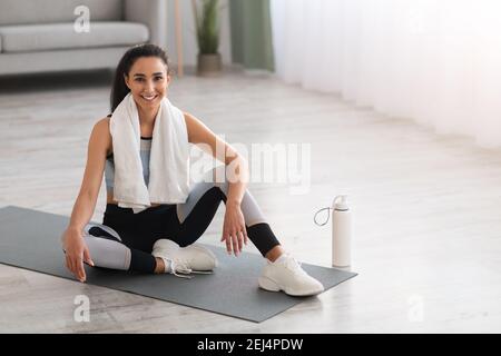 Attractive lady in sportswear sitting on yoga mat, resting Stock Photo
