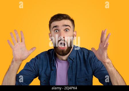 Portrait of shocked man with open mouth looking at camera in amazement, making surprised gesture over orange background Stock Photo