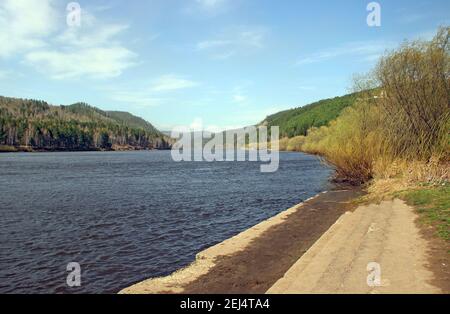 Wide concrete steps lead to the river. There is an amazing view of the water ripples and wooded hills in the distance. Stock Photo