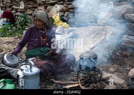 Elderly woman, Tibetan, preparing tea water at a smoking wood fire, Dolpo, Nepal Stock Photo