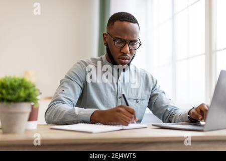 Black Businessman Taking Notes Sitting Working At Workplace In Office Stock Photo
