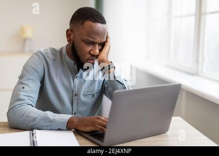 Unhappy Black Businessman Looking At Laptop Sitting At Workplace Indoor Stock Photo
