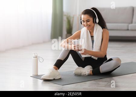 Happy young woman resting on yoga mat, listening to music Stock Photo