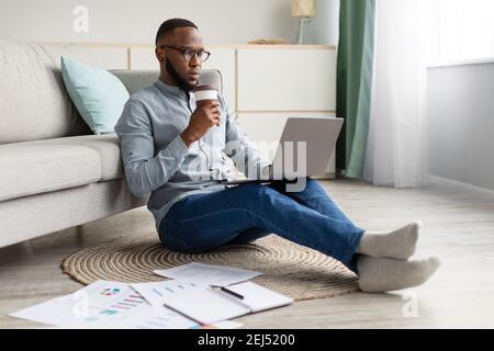 Black Man Working On Laptop Sitting On Floor At Home Stock Photo