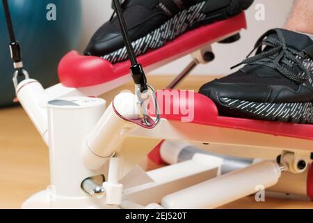Close up mans feet in sneakers training on the twist stepper with digital display and gum expanders at home during lockdown.  Stock Photo