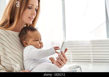 Cute infant baby daughter learning using phone with mom at home. Stock Photo