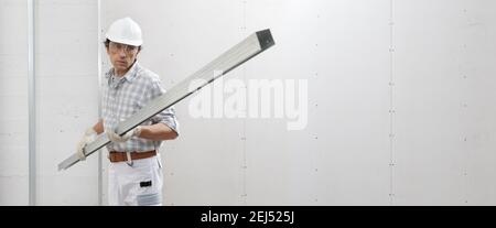man worker with drywall metal profile for installing plasterboard sheet to wall. Wearing white hardhat, work gloves and safety glasses. Isolated on wh Stock Photo