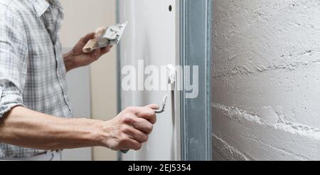 closeup hands man drywall worker or plasterer putting stucco on plasterboard wall using a trowel and a spatula, fill the screw holes Stock Photo