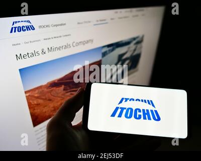 Person holding cellphone with company logo of Japanese conglomerate Itochu Corporation on screen in front of business website. Focus on phone display. Stock Photo