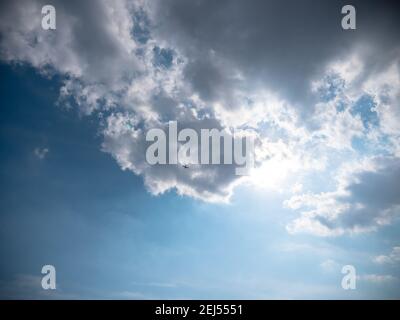 Airplane flying high up in the sky below dark blue stormy clouds with sun shining through them. Stock Photo