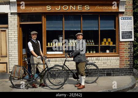 Beautiful gay couple at sunny day riding bike.Gay male couple standing beside retro bicycle in from of old bakery in Shoreditch, East London , England