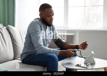 Black Young Man Measuring Arterial Pressure Feeling Bad At Home Stock Photo