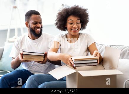 Black Spouses Packing Books In Boxes Moving To New Apartment Stock Photo