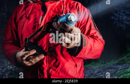 Photo of hiker man in red travel camping jacket holding shining head flashlight. Stock Photo