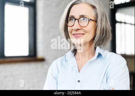 Headshot portrait of a charming smiling elegant senior woman in glasses standing and looking away, thinking of the bright company future. Close-up of Stock Photo