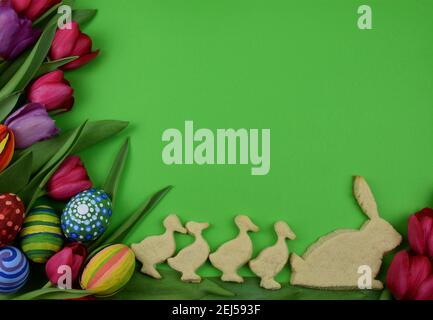 tulips, painted eggs and bunny and chick  shaped cookies on green background Stock Photo