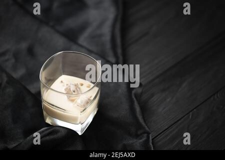 Glass of Irish cream baileys liqueur with ice cubes on dark fabric and wooden bar table background. Homemade luxury elite alcohol cocktail. Place for Stock Photo