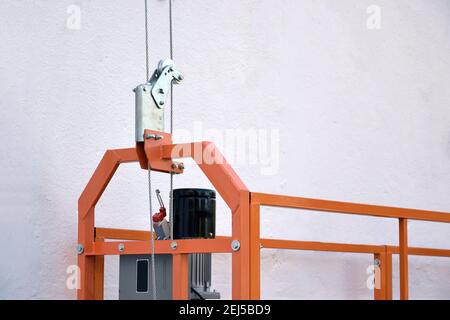 Hoist supply and safety lock as part of suspended wire rope platform for facade works on high multistorey buildings. Hoist for elevation, raising or l Stock Photo