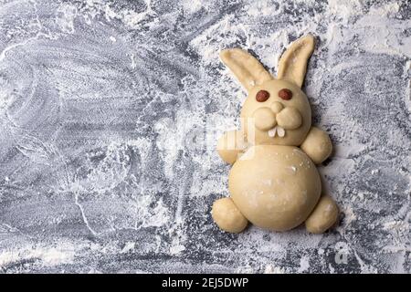 Raw Easter Bunny Buns of delicious sweet dough on a table sprinkled with flour, top view, space Stock Photo