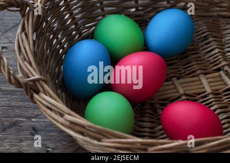 Colored easter eggs in a wicker basket on a wooden surface Stock Photo
