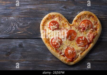 Homemade delicious margarita pizza with tomatoes in the shape of a heart on a wooden table for Valentine's Day, top view, space Stock Photo