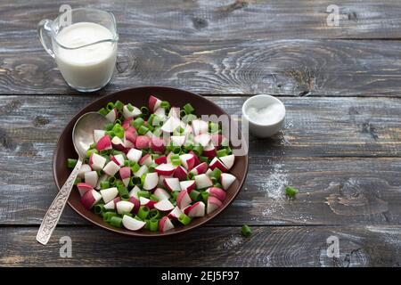 Fresh radish salad with green onions and sour cream on a wooden background, rustic style. Delicious homemade food Stock Photo