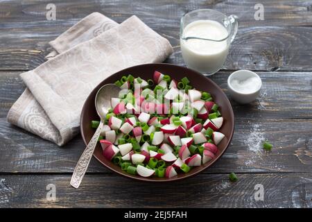 Fresh radish salad with green onions and sour cream on a wooden background, rustic style. Delicious homemade food Stock Photo