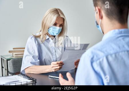 Female hr manager, employer wearing face mask reading cv at job interview. Stock Photo