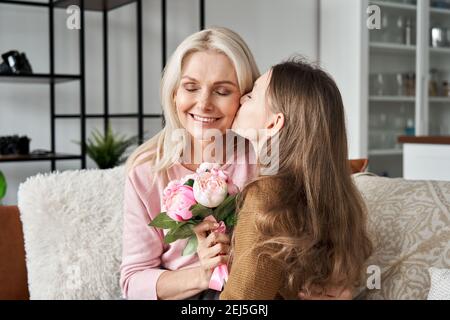 Cute teen child daughter presenting spring flowers kissing mom on Mothers Day. Stock Photo
