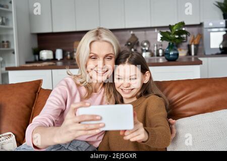 Happy teen child daughter and middle aged mother having fun using smartphone. Stock Photo