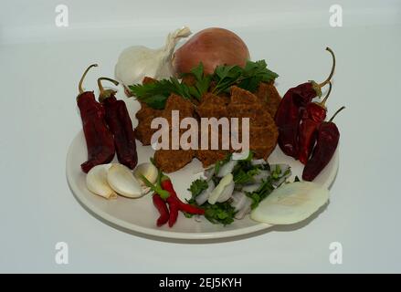 raw meatballs on white big plate, presentation composition made of spicy sauce in the middle beside lemon tomato greens mint macro shot meal Turkish. Stock Photo