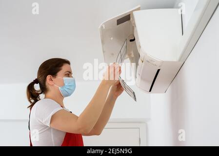 Female technician wearing face mask and cleaning air conditioner Stock Photo