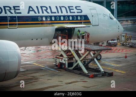 A ULD loader lifting a unit load device (ULD) from apron dollies to an aircrafts cargo bay of a Singapore Airlines machine at Changi Airport Singapore