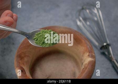 Vertical image matcha tea powder pouring in wooden bowl on Gray Stone Background. Japanese Green Tea Concept. Matcha Tea Preparation Ingredient 2021. Stock Photo