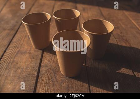 Disposable dark brown kraft paper cups stand on wooden table against brown background Stock Photo