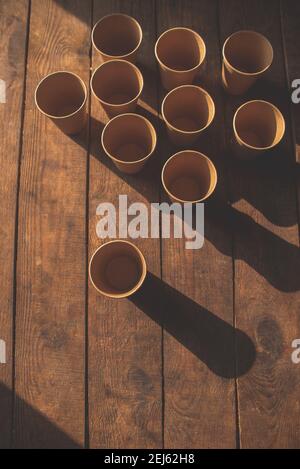 Disposable dark brown kraft paper cups stand on wooden table against brown background Stock Photo