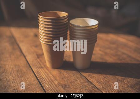 disposable cups made of dark brown paper and white cups stand on wooden table against brown background Stock Photo