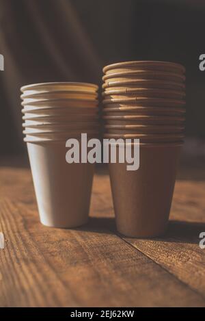 disposable cups made of dark brown paper and white cups stand on wooden table against brown background Stock Photo