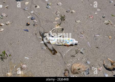 Used Tooothpaste tube discarded on shells beach ecosystem,sea coast pollution contamination Stock Photo
