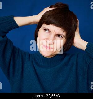 Portrait of mature woman in distress, close-up. Agitated tensed face. Bright dark blue wall Stock Photo