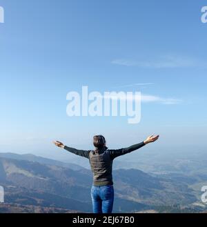 Freedom and relaxation. Young woman raises her hands up while standing on a high mountain. Stock Photo