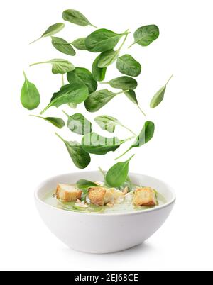 Bowl with tasty soup and falling spinach leaves on white background Stock Photo