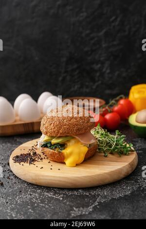 Tasty burger with florentine egg and fresh vegetables on dark background Stock Photo
