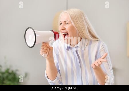 Screaming mature woman with megaphone at home Stock Photo